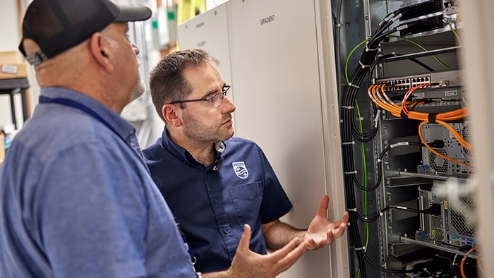 Two men in maintenance worker outfits look at a server rack