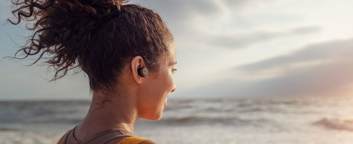 Kvinne som bruker trådløse hodetelefoner ved sjøen