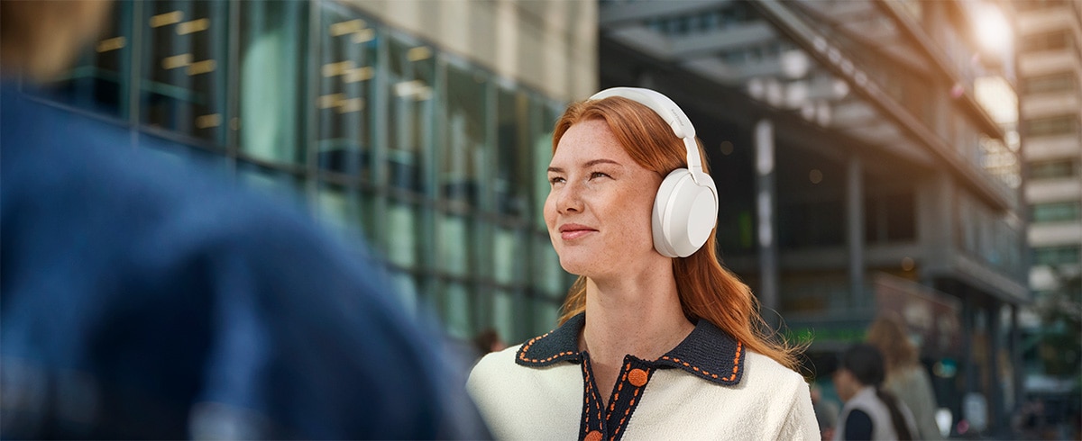 Person med Philips TAH8000EWT over-ear hodetelefoner utendørs i et urbant miljø