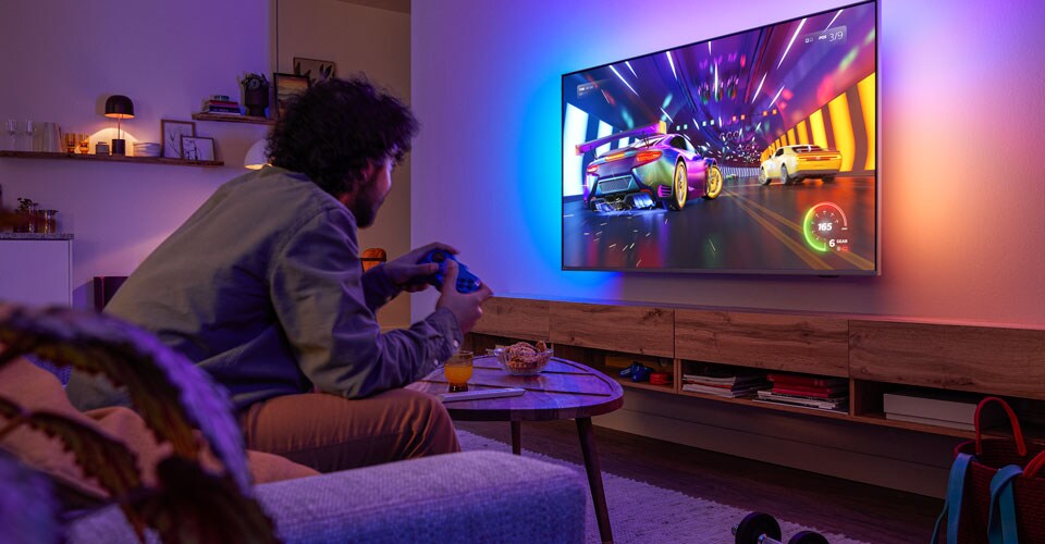 En person sitter i en sofa og spiller et racingspill på en Philips Ambilight-TV
