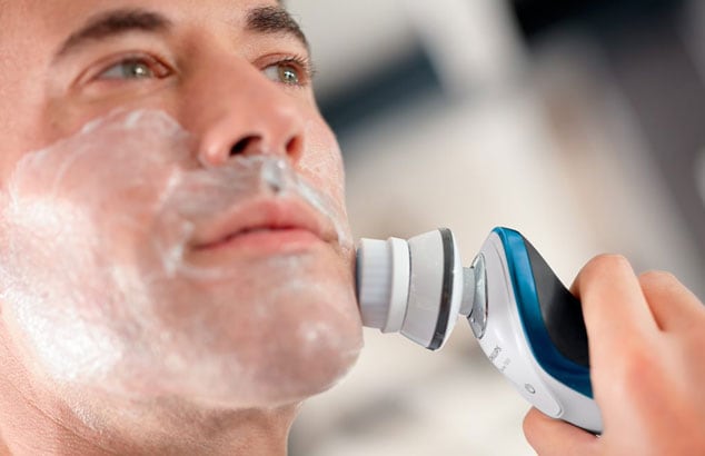 Nærbilde av en manns ansikt med barberskum i ansiktet og en elektrisk børste mot kinnet.
