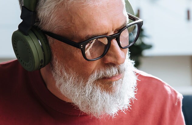 Nærbilde av en eldre mann med hvitt hår og hvitt skjegg iført hodetelefoner som spiller gitar