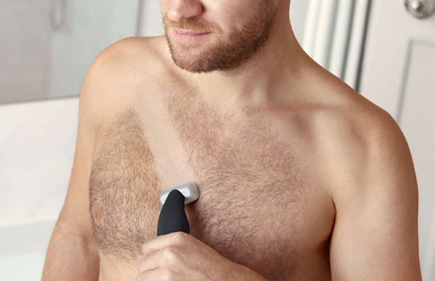 Nærbilde av en manns hårete bryst med stripe som blir barbert på tvers av en barbermaskin han holder.