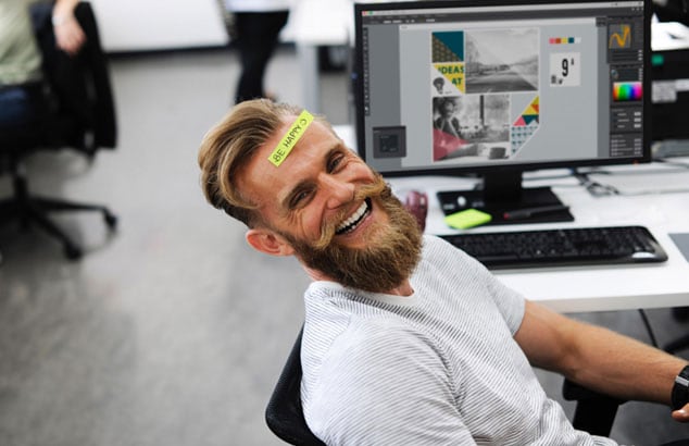 Blond, ung fyr med stort skjegg sitter på en kontorstol og smiler til kameraet.