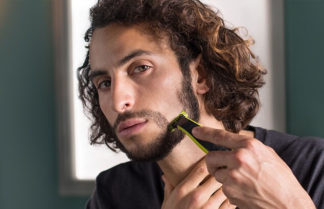 En mann barberer en del av skjegget vertikalt, og begynner å forme det til fippskjegg.