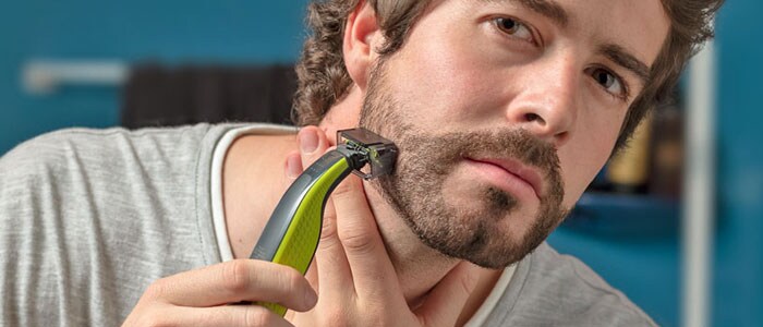 En mann trimmer marginen på skjegget ved hjelp av en trimmer med spesielt tilbehør