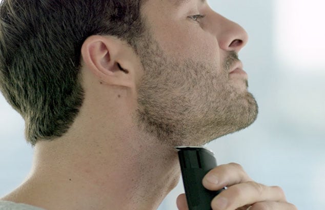 Sideprofil av en mann med kort skjegg som barberer halsen med en arbermaskin.