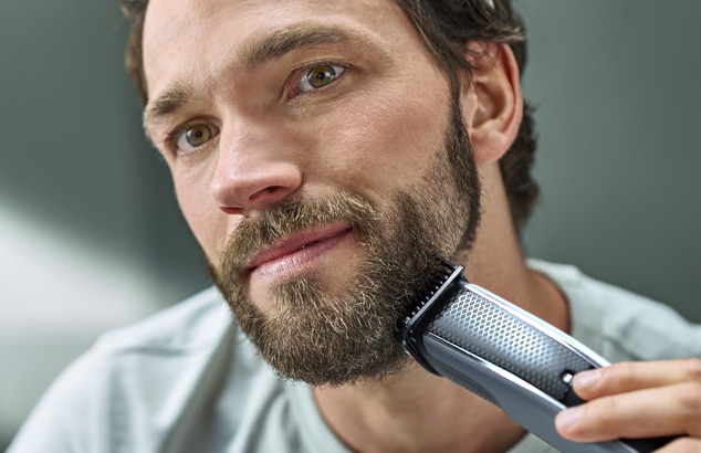 En mann med helskjegg barberer ansiktet med en svart- og sølvfarget barbermaskin.