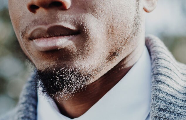 Nærbilde av en svart mann i en hvit skjorte og grå cardigan og med soul patch-skjegg