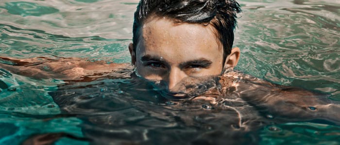 Mann med mørkt vått hår i klart vann har kun øverste halvdel av hodet over vannet og ser intenst inn i kamera