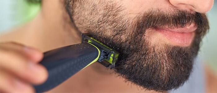 Nærbilde av en brunøyd mann som barberer seg og trimmer det mørke skjegget med Philips OneBlade.
