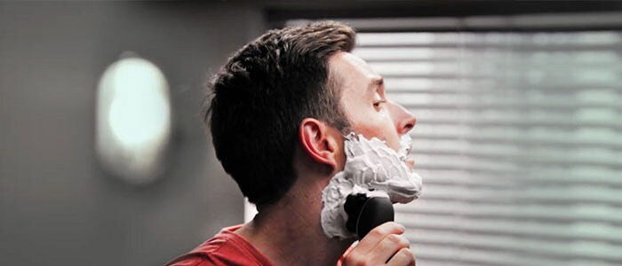 En mann med barberskum i ansiktet barberer seg med en barbermaskin.