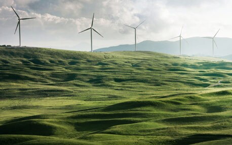 Et bilde av en grønn åsside med vindturbiner som går rundt for å skape fornybar energi i bakgrunnen.